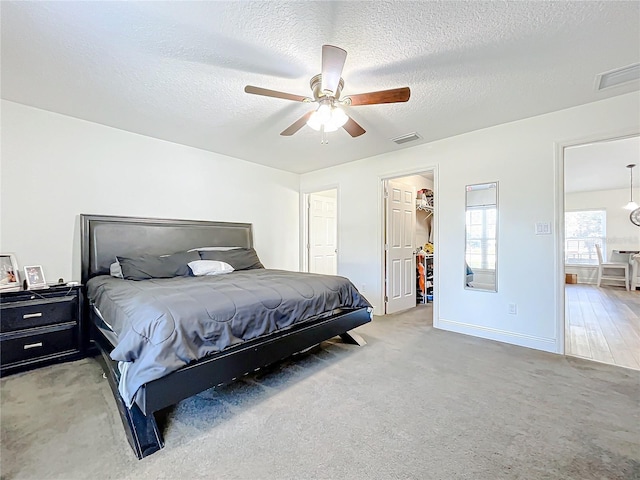 bedroom with carpet flooring, a textured ceiling, a walk in closet, and ceiling fan