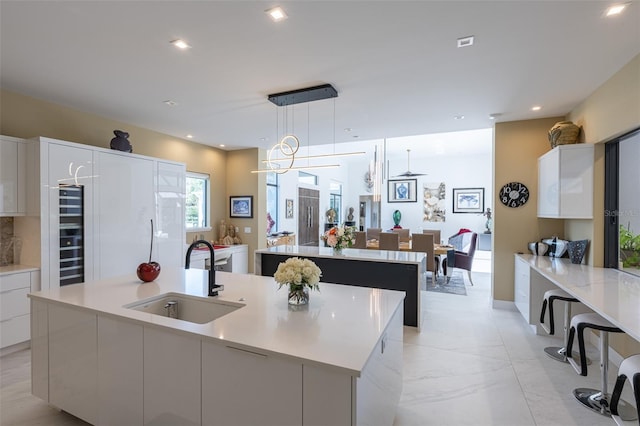 kitchen with sink, built in refrigerator, pendant lighting, a spacious island, and white cabinets