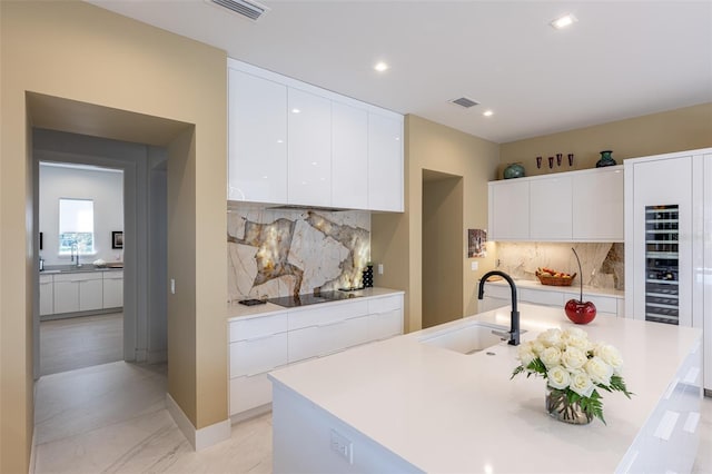 kitchen with decorative backsplash, black electric cooktop, sink, a center island with sink, and white cabinetry