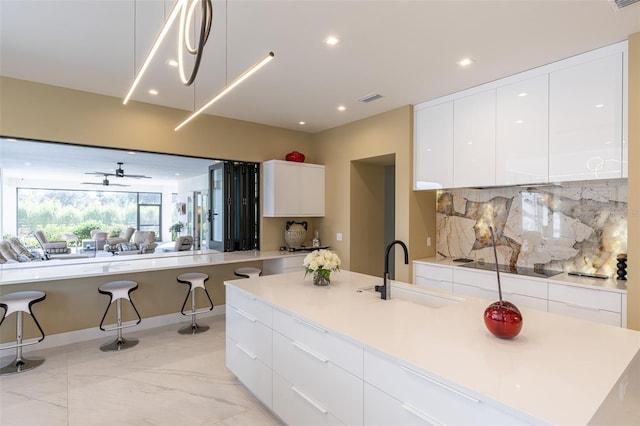 kitchen with a large island with sink, white cabinets, sink, ceiling fan, and tasteful backsplash