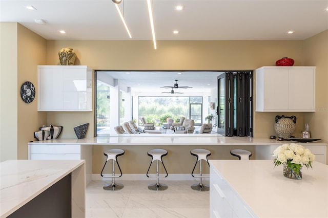 kitchen with white cabinets, ceiling fan, light stone countertops, and a breakfast bar area