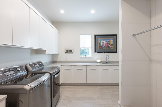 washroom featuring cabinets, light hardwood / wood-style floors, washing machine and dryer, and sink