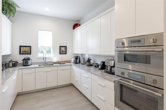 kitchen with white cabinets, light hardwood / wood-style floors, double oven, and sink