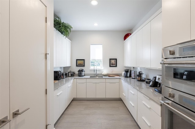 kitchen with kitchen peninsula, stainless steel double oven, sink, light hardwood / wood-style floors, and white cabinetry