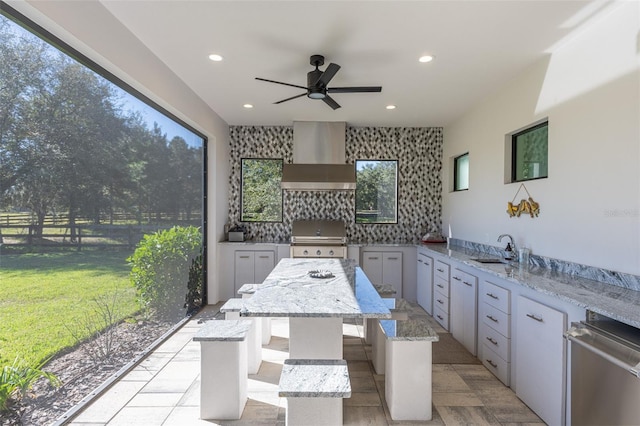 kitchen featuring light stone countertops, a center island, wall chimney exhaust hood, sink, and white cabinets