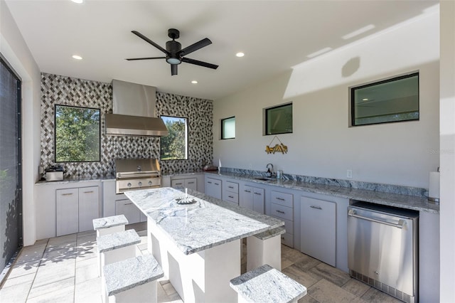 kitchen featuring a center island, stainless steel dishwasher, a wealth of natural light, and wall chimney range hood