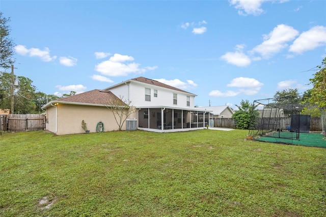 rear view of property featuring central AC unit, a sunroom, a trampoline, and a lawn