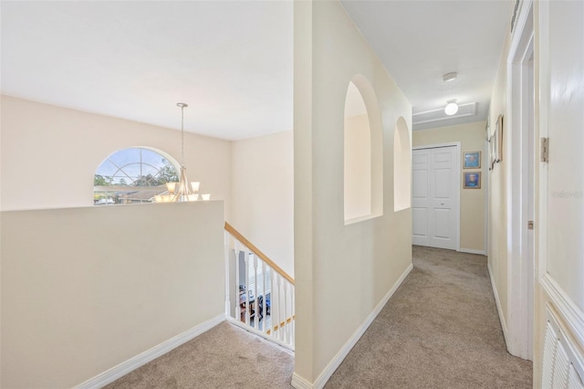 corridor featuring light carpet and an inviting chandelier