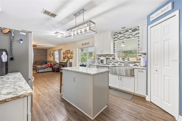 kitchen with white cabinets, pendant lighting, a kitchen island, and sink