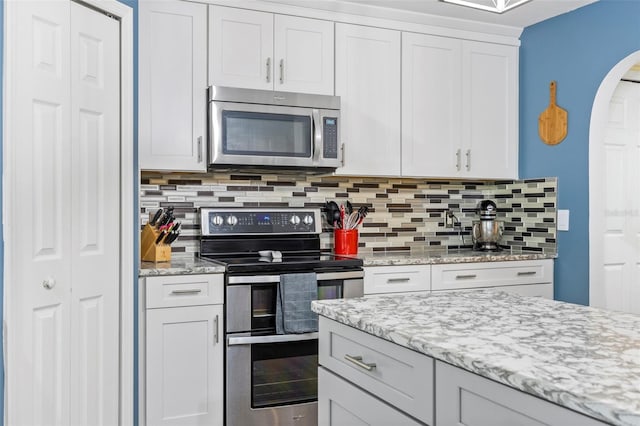 kitchen featuring decorative backsplash, stainless steel appliances, white cabinetry, and light stone countertops