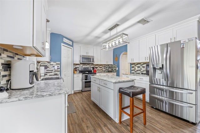 kitchen featuring stainless steel appliances, sink, decorative light fixtures, white cabinets, and a center island