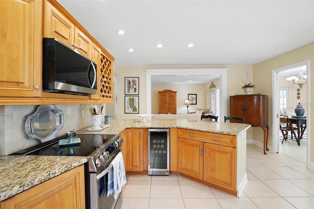 kitchen with light stone countertops, beverage cooler, stainless steel appliances, kitchen peninsula, and decorative backsplash