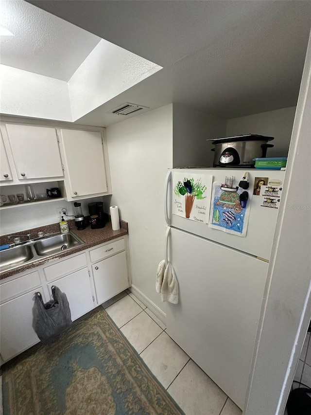 kitchen featuring a textured ceiling, sink, light tile patterned floors, white refrigerator, and white cabinetry