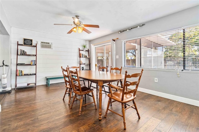 dining space featuring ceiling fan, plenty of natural light, dark wood-type flooring, and wooden walls