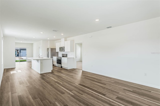 kitchen with appliances with stainless steel finishes, dark wood-type flooring, sink, white cabinets, and an island with sink