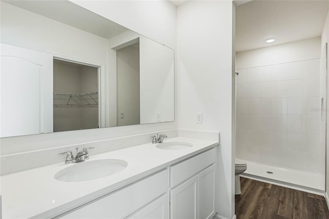 bathroom featuring a tile shower, vanity, wood-type flooring, and toilet