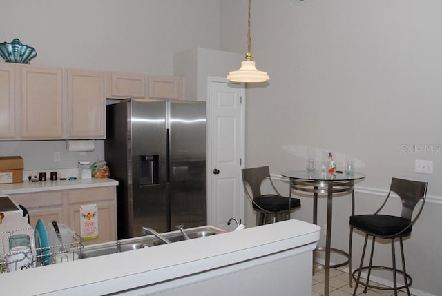 kitchen with stainless steel fridge with ice dispenser, light brown cabinetry, light tile patterned floors, and pendant lighting