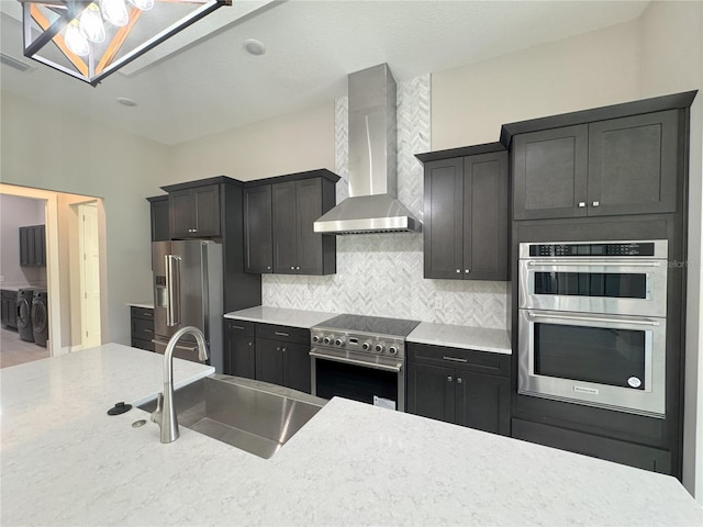 kitchen featuring backsplash, sink, wall chimney exhaust hood, independent washer and dryer, and stainless steel appliances