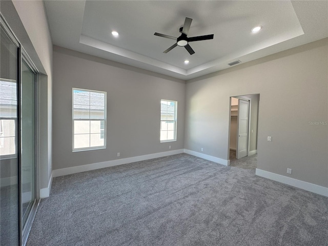 unfurnished bedroom featuring carpet flooring, a tray ceiling, a spacious closet, and ceiling fan