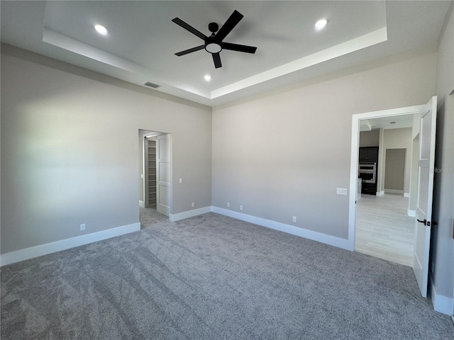 spare room featuring a tray ceiling, ceiling fan, and light colored carpet