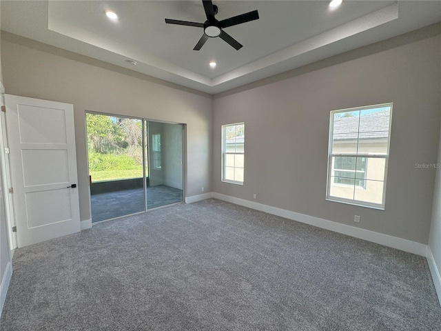 carpeted spare room with a raised ceiling and ceiling fan