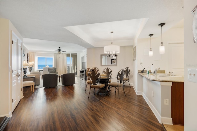 dining space with hardwood / wood-style flooring, ceiling fan with notable chandelier, sink, and a tray ceiling