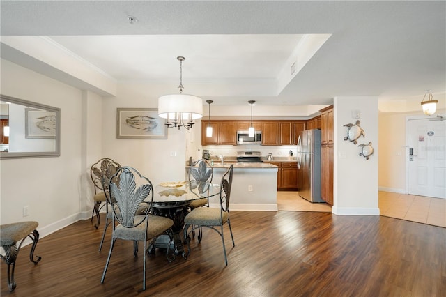 dining room with sink, crown molding, a tray ceiling, wood-type flooring, and a chandelier