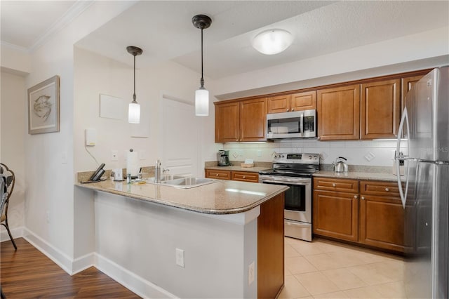 kitchen with kitchen peninsula, stainless steel appliances, sink, pendant lighting, and light hardwood / wood-style flooring