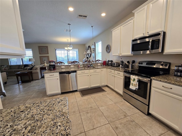 kitchen with kitchen peninsula, appliances with stainless steel finishes, pendant lighting, an inviting chandelier, and dark stone countertops