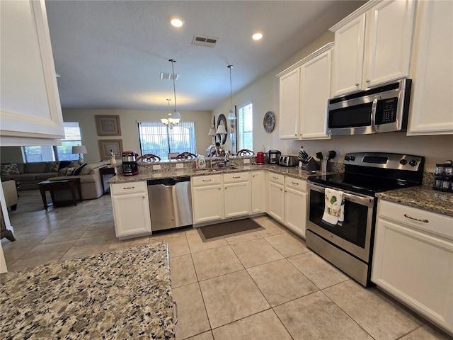 9037 Shadow Mountain St, Davenport, FL 33896 - kitchen with appliances with stainless steel finishes, a peninsula, white cabinetry, a chandelier, and dark stone countertops