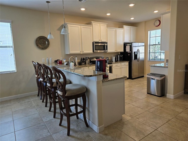 kitchen featuring a kitchen breakfast bar, kitchen peninsula, pendant lighting, white cabinets, and appliances with stainless steel finishes