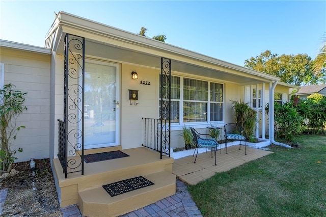 view of exterior entry with a lawn and a porch