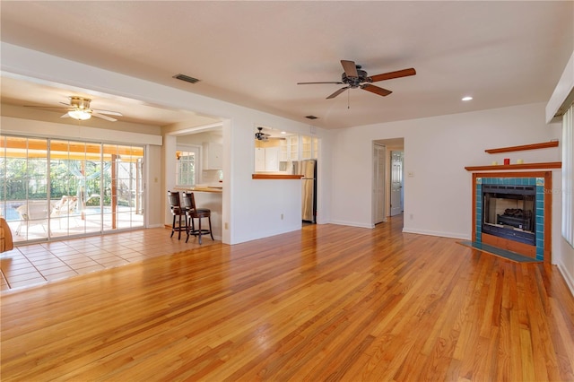 unfurnished living room featuring a tile fireplace, light wood-type flooring, and ceiling fan