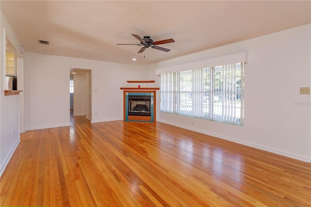 unfurnished living room with a tiled fireplace, ceiling fan, and light hardwood / wood-style floors