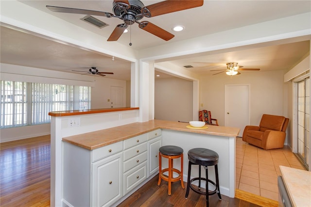 kitchen featuring white cabinets, hardwood / wood-style flooring, kitchen peninsula, and a breakfast bar area