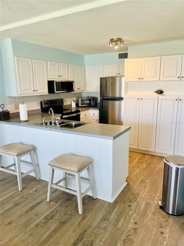 4501 S Atlantic Ave Unit 4090, New Smyrna Beach, FL 32169 - kitchen featuring stainless steel appliances, a peninsula, light wood-style floors, a breakfast bar, and white cabinets
