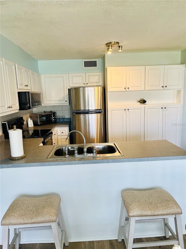 4501 S Atlantic Ave Unit 4090, New Smyrna Beach, FL 32169 - kitchen with freestanding refrigerator, black / electric stove, backsplash, a breakfast bar, and white cabinetry
