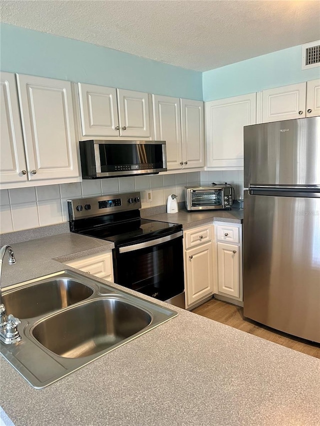 4501 S Atlantic Ave Unit 4090, New Smyrna Beach, FL 32169 - kitchen featuring stainless steel appliances, white cabinetry, light wood finished floors, backsplash, and a textured ceiling