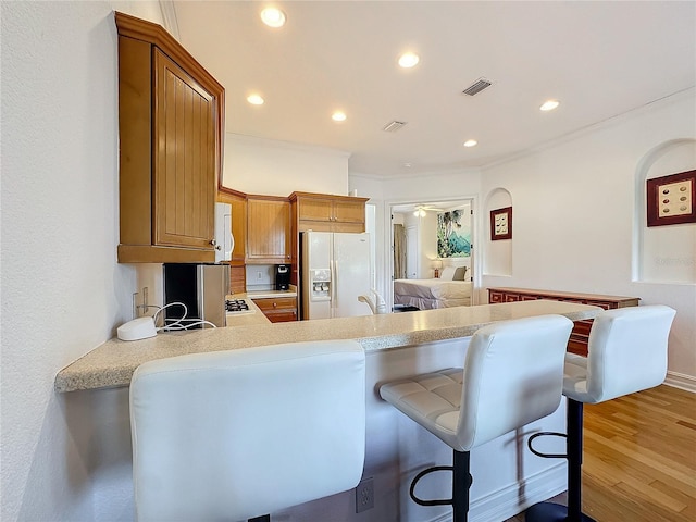 kitchen featuring white appliances, light hardwood / wood-style flooring, ornamental molding, a kitchen bar, and kitchen peninsula