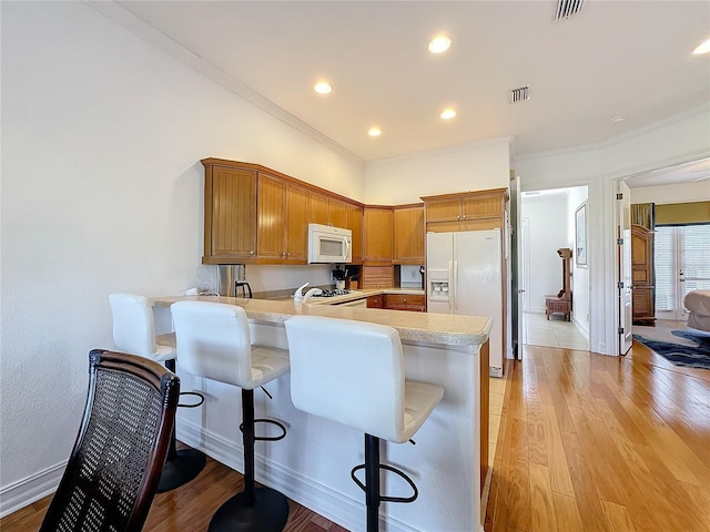 kitchen with white appliances, a breakfast bar, kitchen peninsula, and light hardwood / wood-style floors