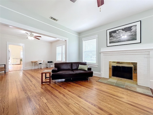 living room with ceiling fan, wood-type flooring, and a brick fireplace