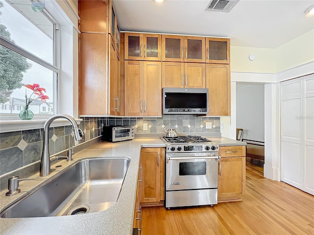 kitchen featuring appliances with stainless steel finishes, backsplash, light hardwood / wood-style flooring, and sink