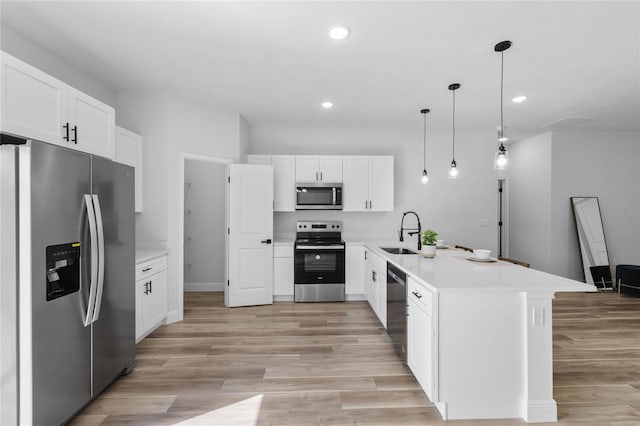 kitchen with pendant lighting, white cabinets, appliances with stainless steel finishes, and light hardwood / wood-style flooring