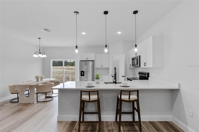 kitchen with a kitchen bar, kitchen peninsula, light wood-type flooring, stainless steel appliances, and white cabinetry