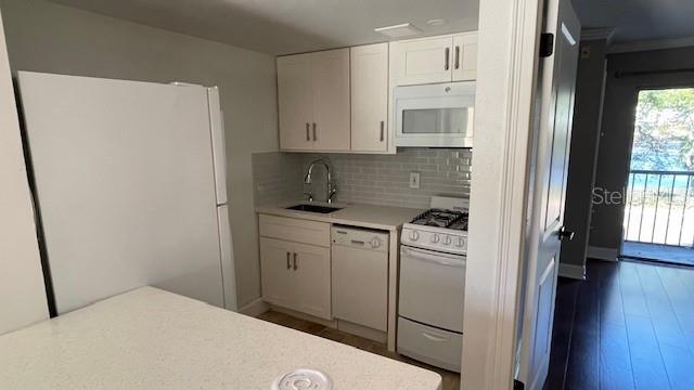 kitchen with white appliances, sink, tasteful backsplash, dark hardwood / wood-style flooring, and white cabinetry