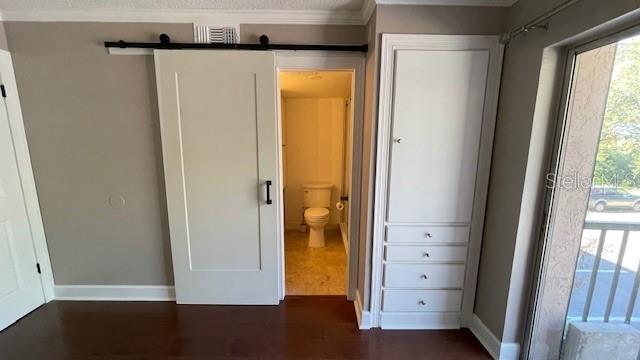 unfurnished bedroom featuring a barn door, dark hardwood / wood-style floors, crown molding, and connected bathroom