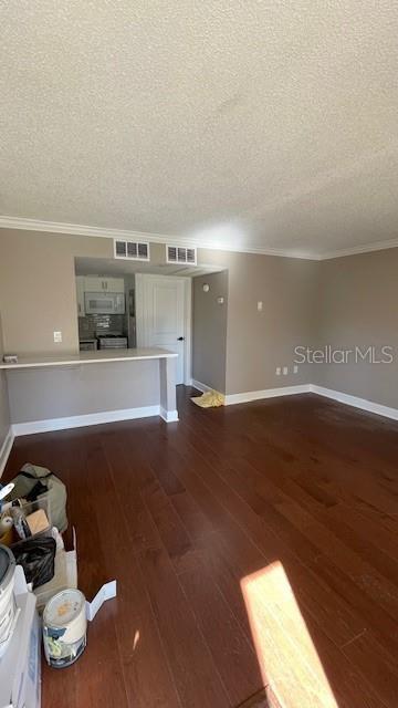 unfurnished living room with dark wood-type flooring, a textured ceiling, and ornamental molding