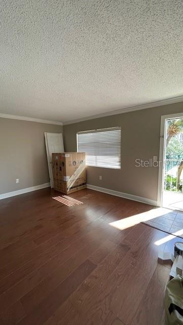 unfurnished living room with a textured ceiling, dark hardwood / wood-style floors, and ornamental molding