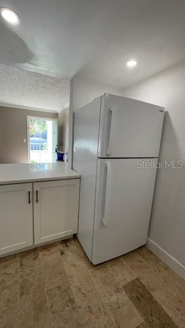 kitchen with white fridge, white cabinetry, and a textured ceiling