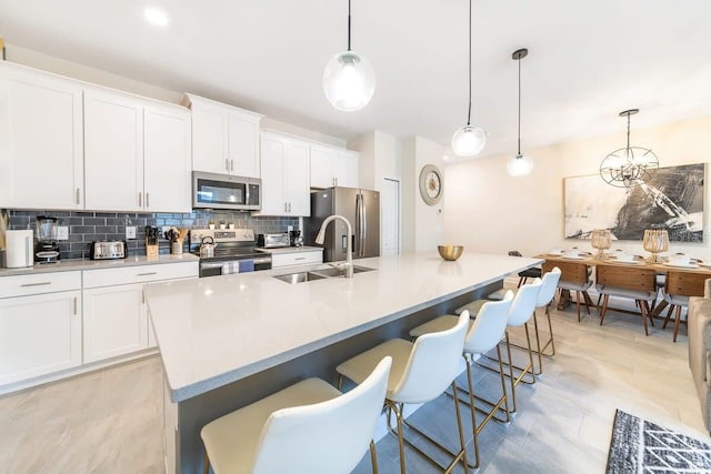 kitchen with white cabinets, pendant lighting, stainless steel appliances, and a center island with sink